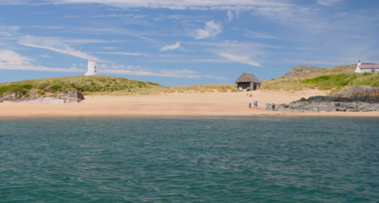 Golden beach at Llanddwyn island with blue skies on a sunny day, blue sea in the foreground